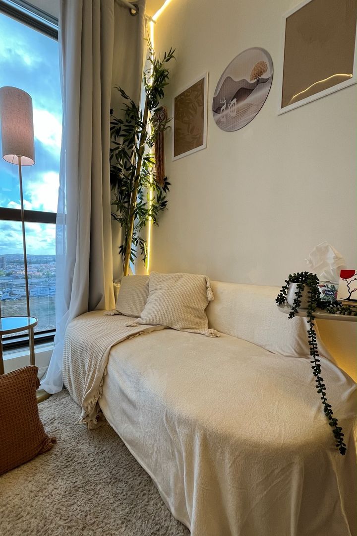 Sofá com manta e almofadas claras, bambu decorativo e quadros na parede ao lado da janela.
