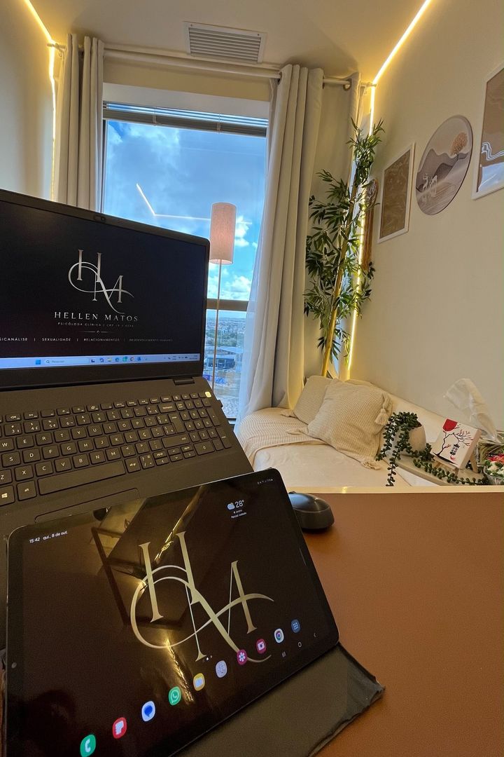 Notebook e tablet exibindo o monograma HM sobre a mesa, com a janela e o sofá ao fundo.