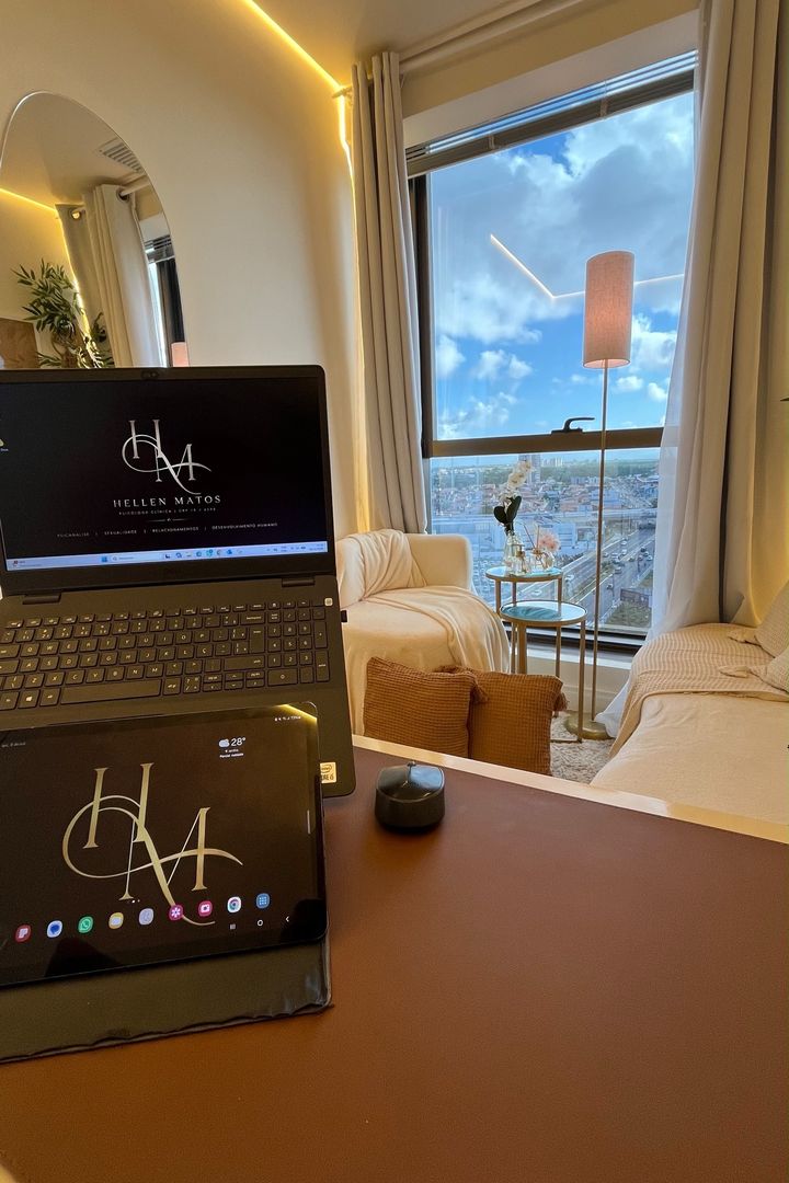 Notebook e tablet com o monograma HM; ao fundo, a janela, o abajur e a poltrona.